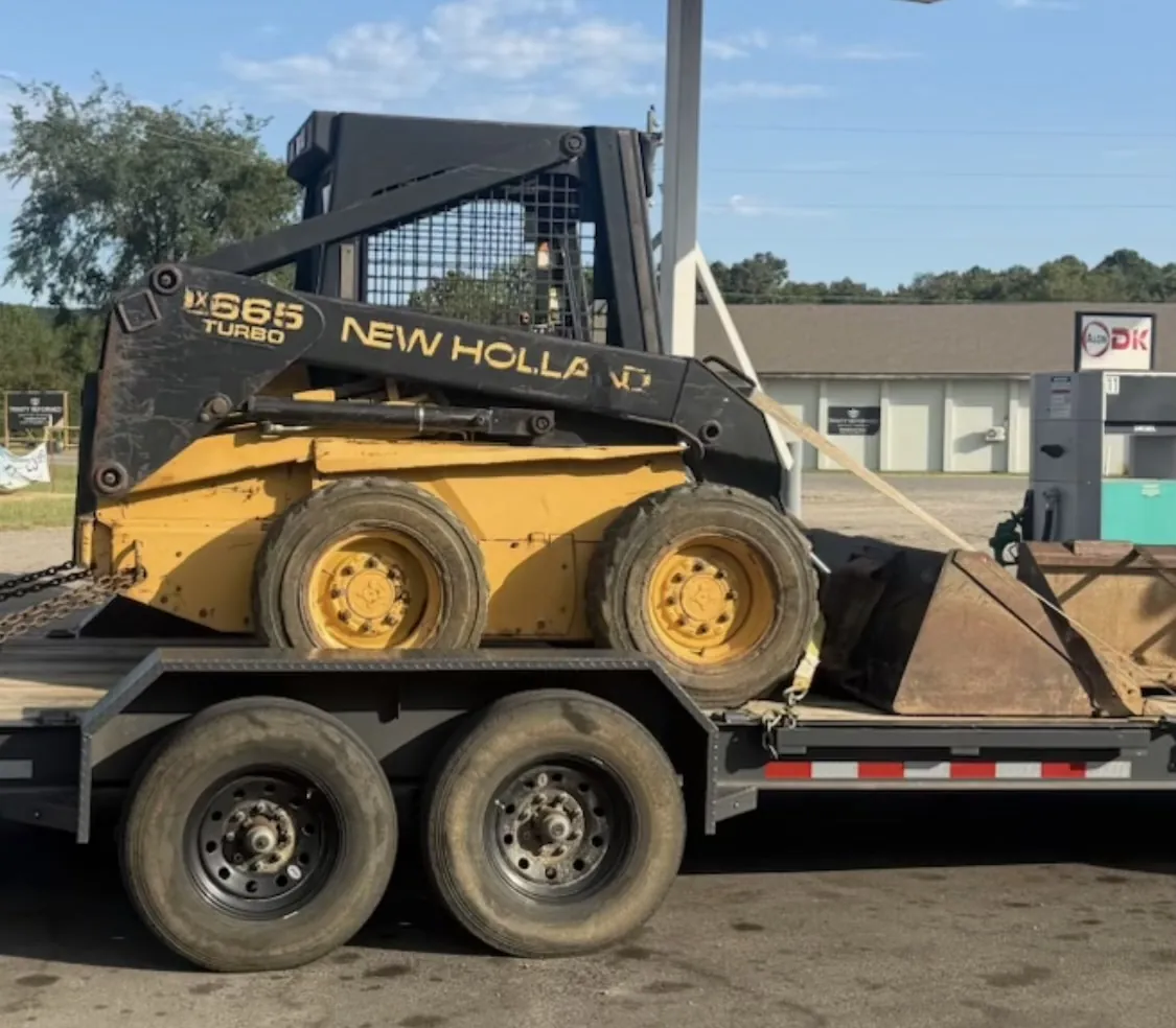 1999 New Holland skid steer and landscaping buckets secured on a trailer