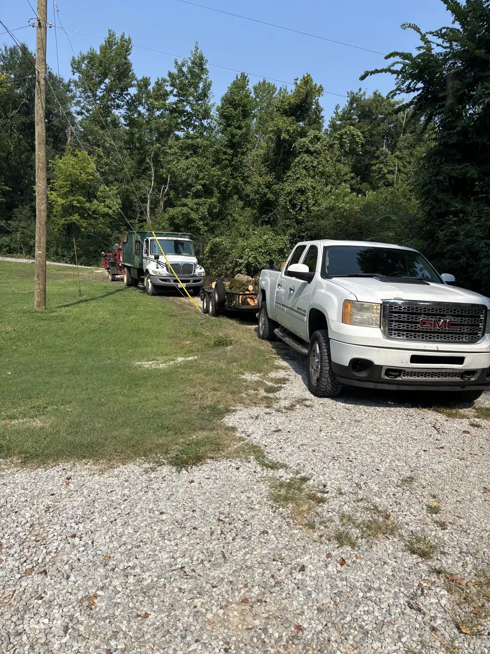 GMC pickup, log trailer, chip truck, and tow-behind wood chipper at a tree-work site